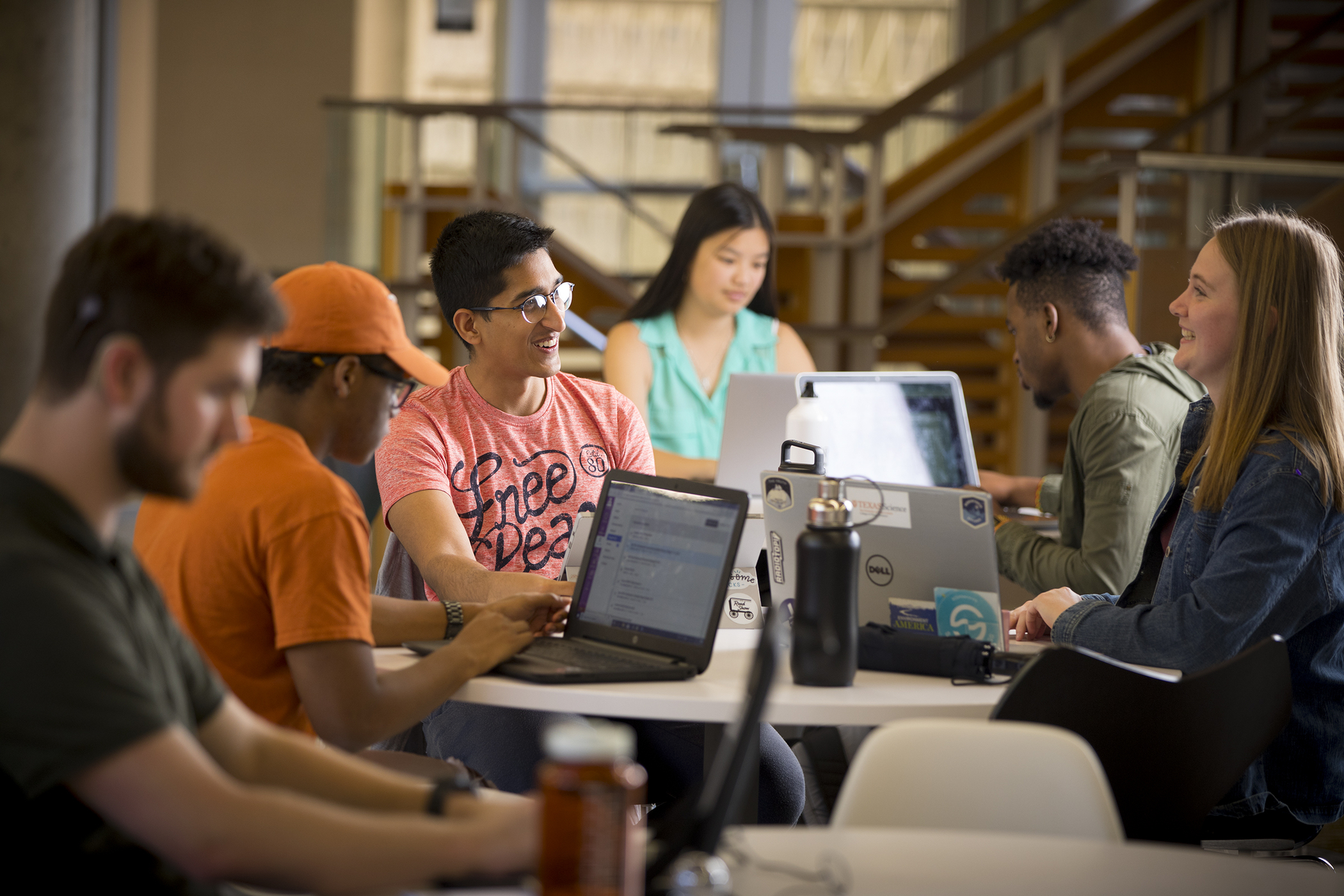several students with laptops around a table smiling